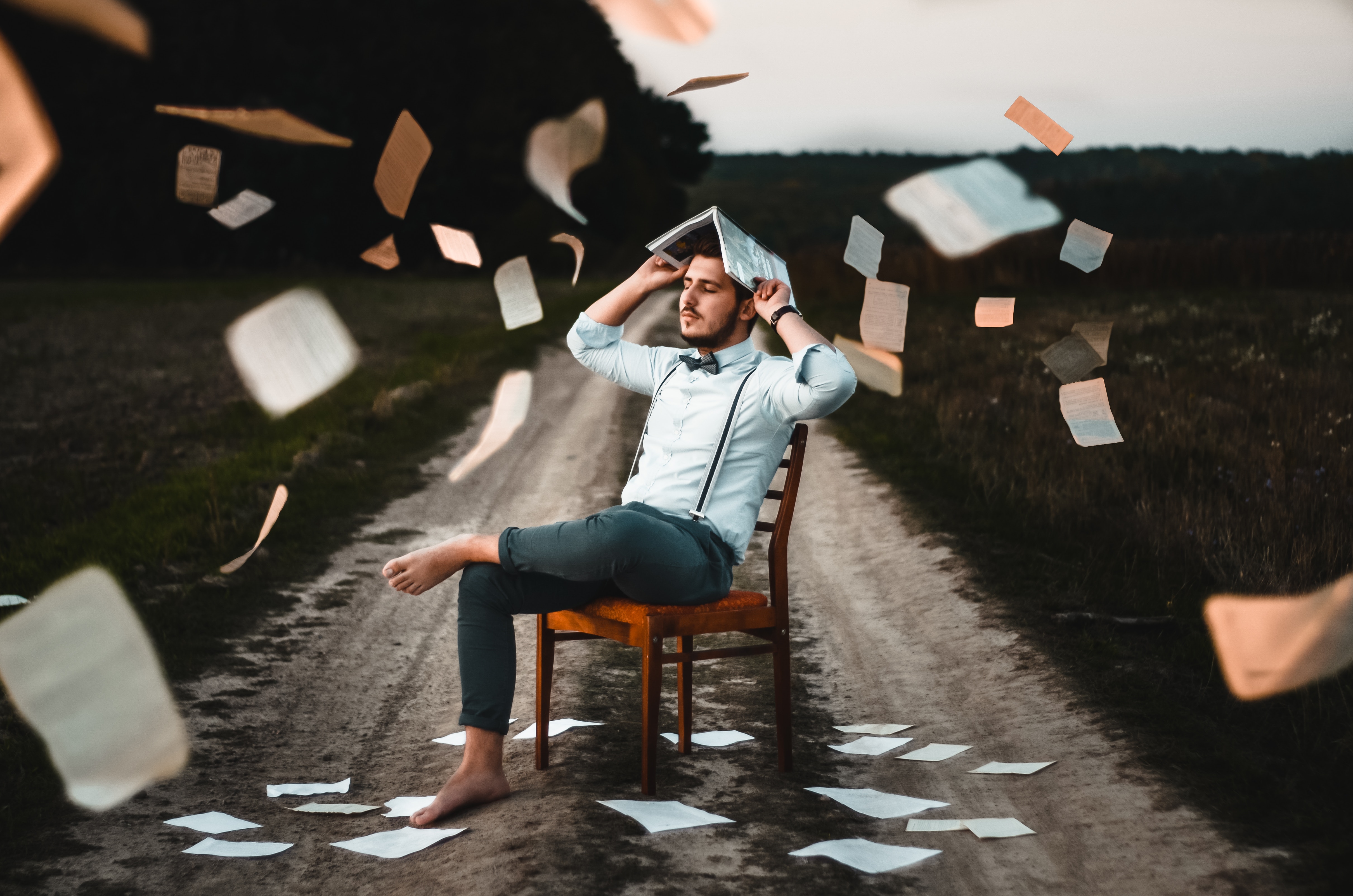 man sitting on a chair with research papers falling on top of his head - burnout concept