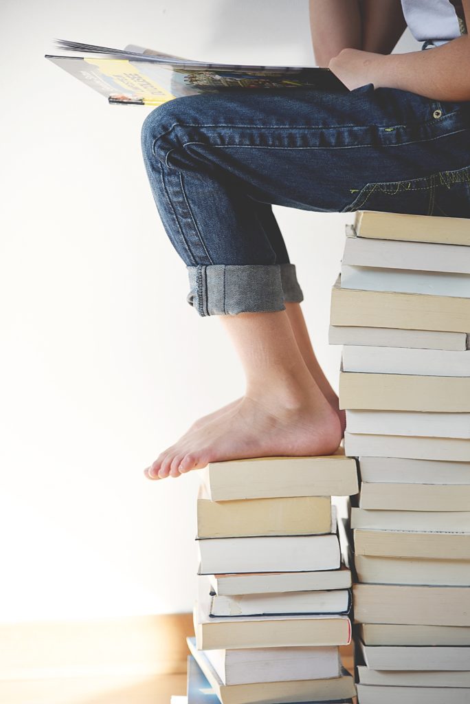 barefoot woman sitting on a large stack of books
