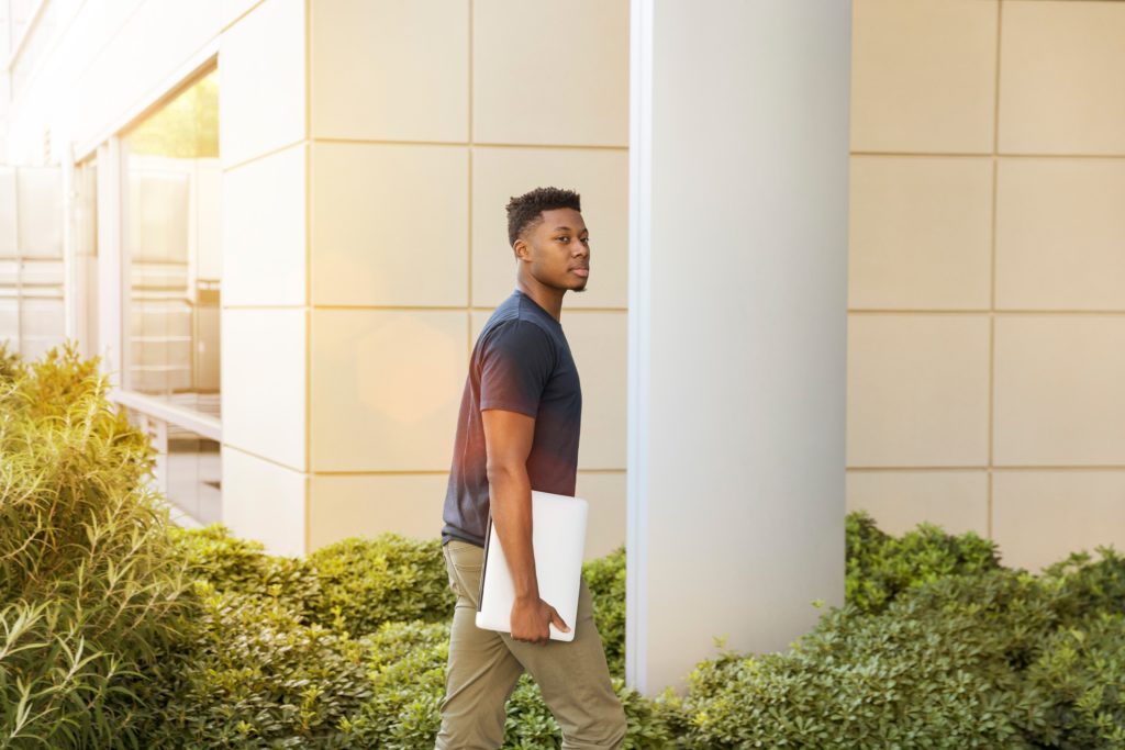 african american student carrying his laptop in college campus