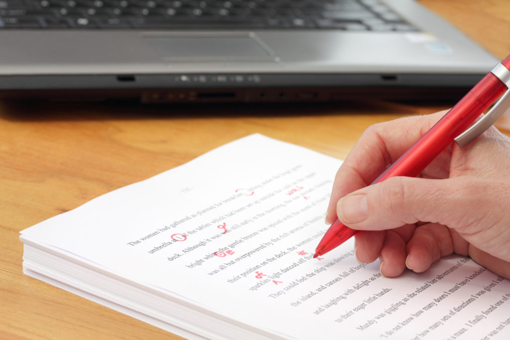 man using a red pen to proofread and mark errors in a book