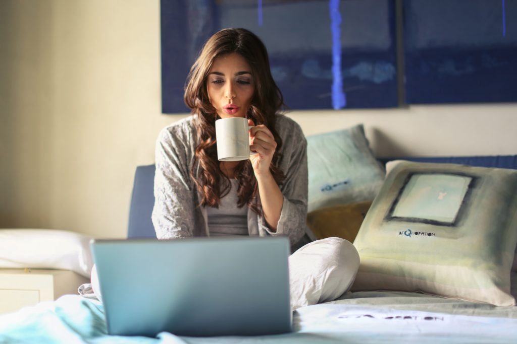 woman drinking a cup of coffee and studying in her bedroom