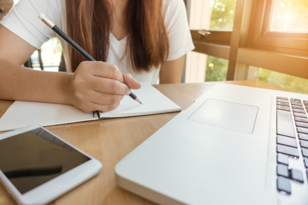 woman taking notes in front of her laptop next to a bright window