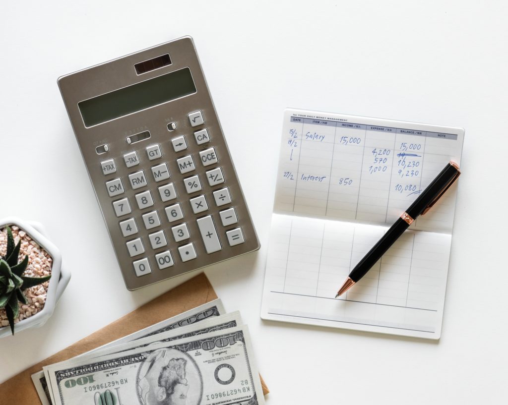 top view of a calculator and dollar bills next to a budget planning notebook