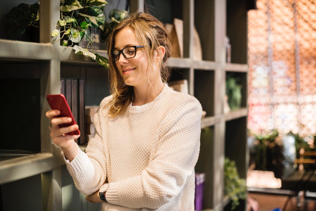 woman in white sweater looking at her phone and smiling