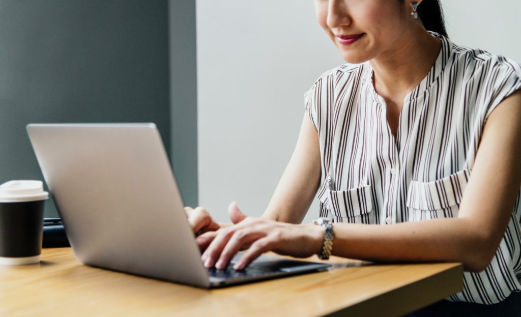 woman in a sleeveless shirt working on her laptop with a cup of coffee