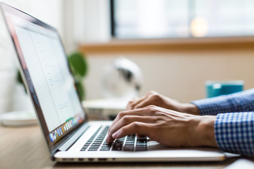 close-up shot of a man in a blue checkered shirt typing on a laptop