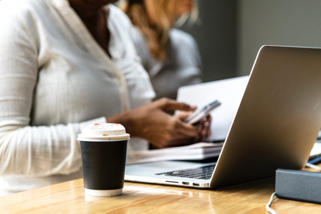 close-up shot of a cup of coffee and a woman checking her phone while working