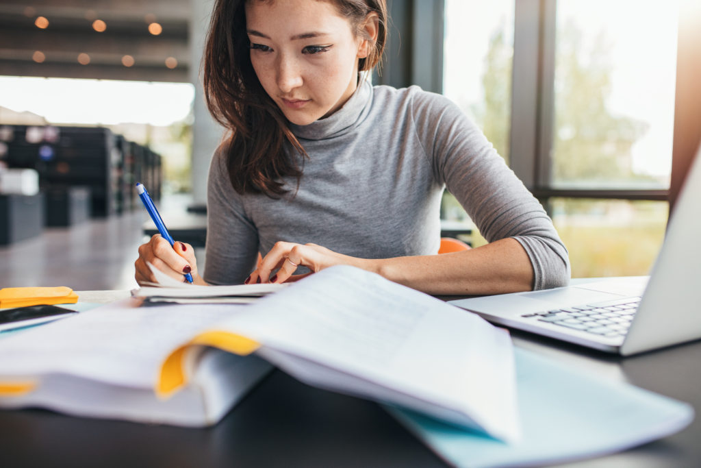 woman in a grey turtleneck sweater studying in a library