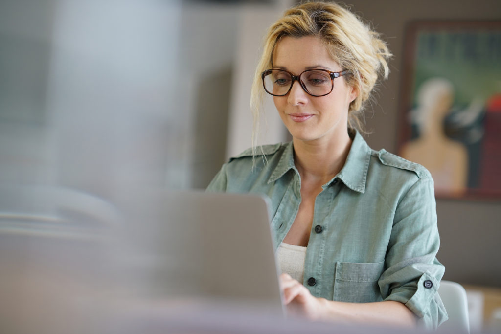 woman with blonde hair and eyeglasses typing on her laptop