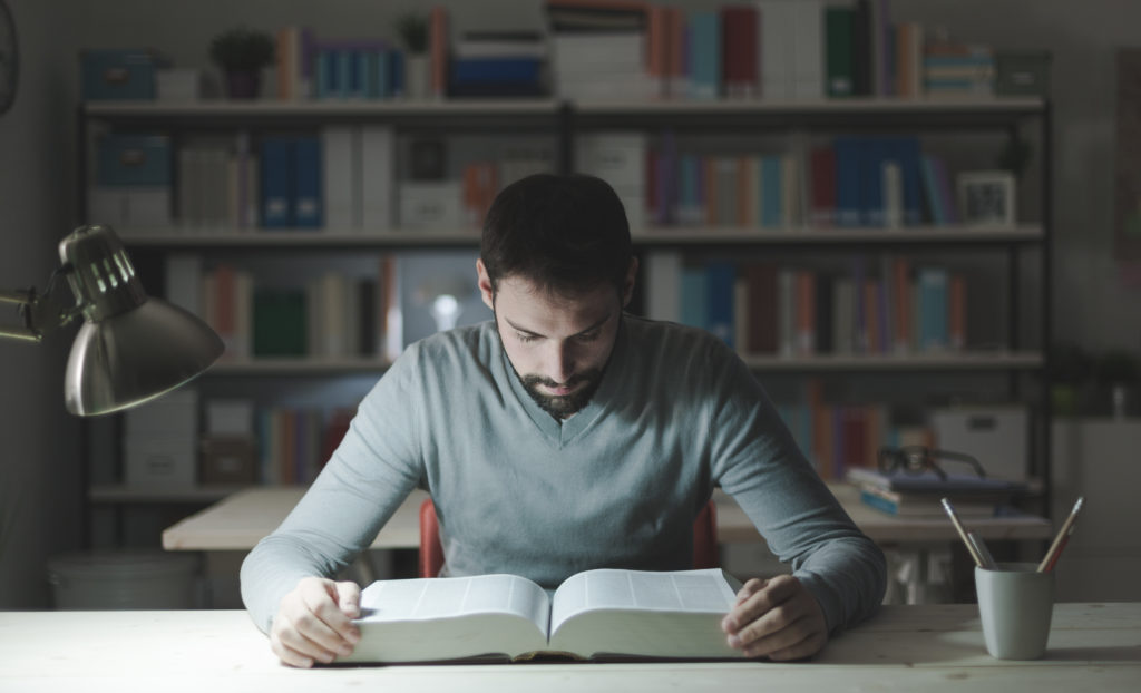 man reading a big book inside a dim library