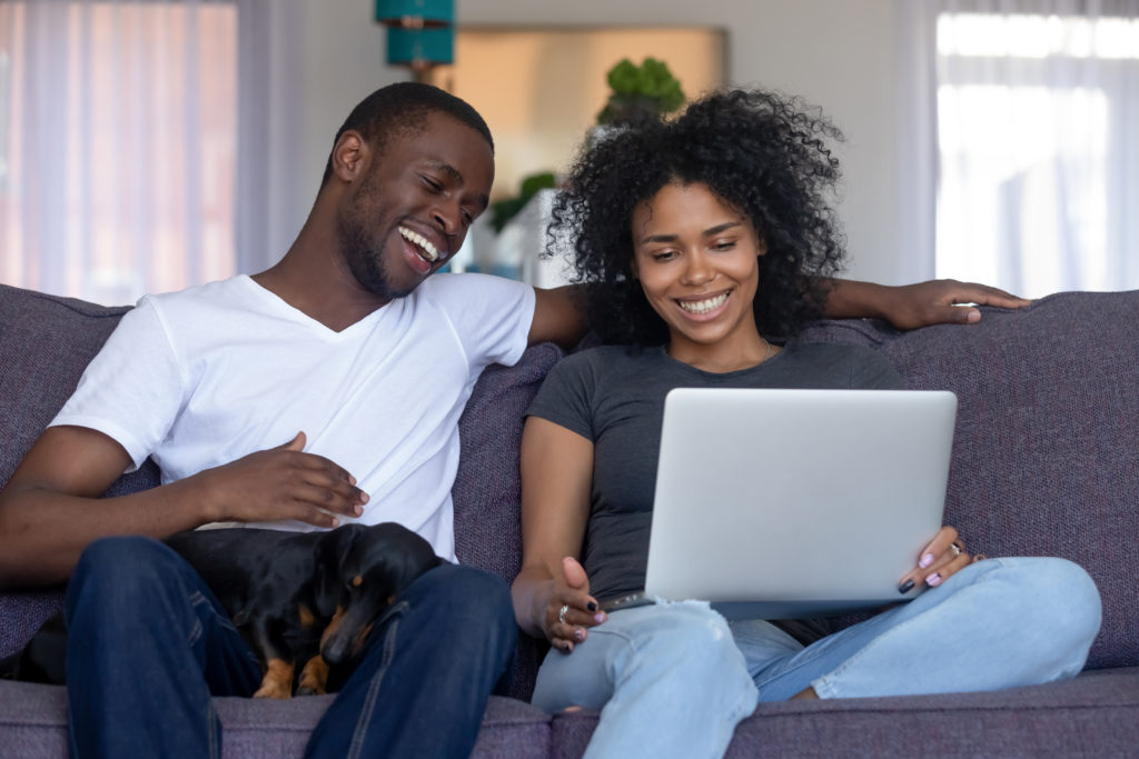 couple laughing on the couch while writing acknowledgments on a laptop