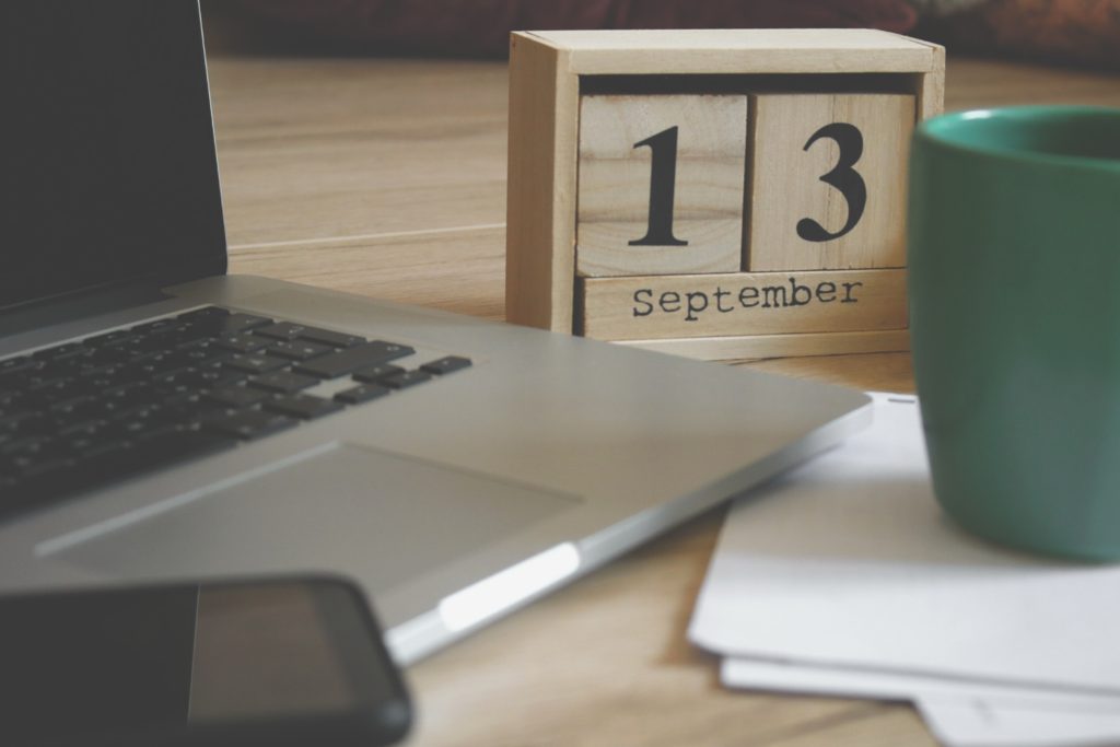 close up shot of a wooden calendar next to a cup of coffee and a laptop