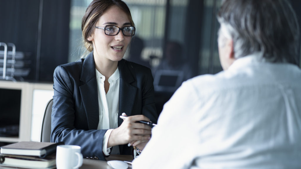 woman in a suit talking to an older man over a cup of coffee