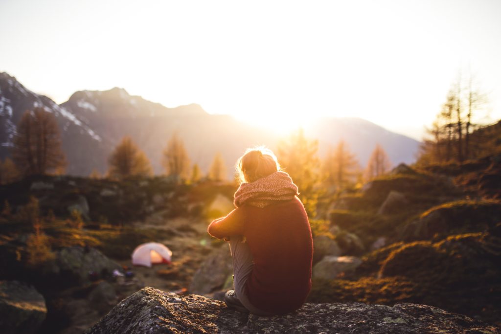 woman sitting alone in the woods looking at the sunset