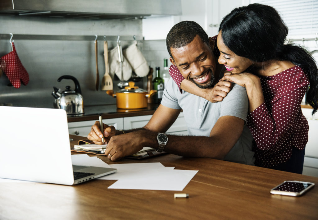 woman hugging her partner while he's studying in their home kitchen