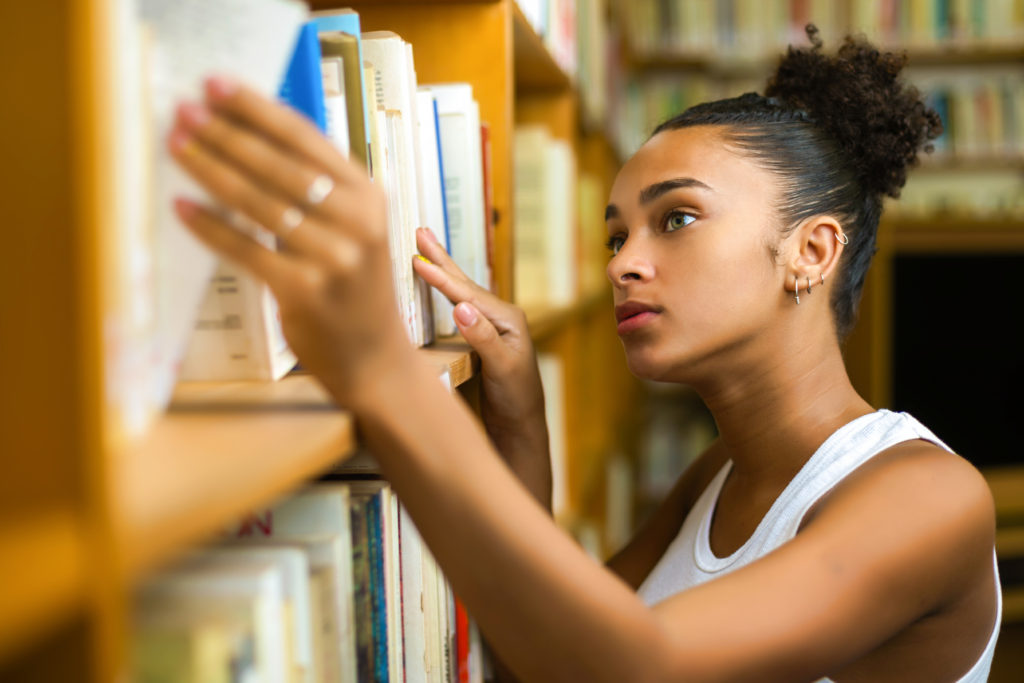 woman with curly hair browsing through books in a library