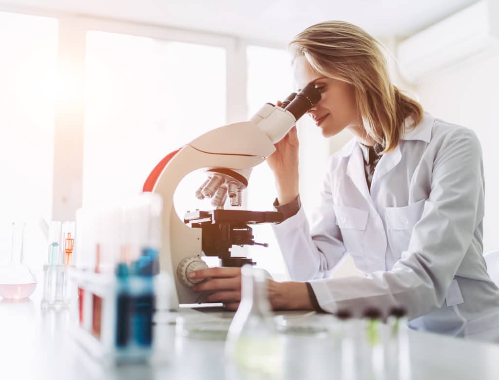 woman in a white lab coat using a microscope to examine materials