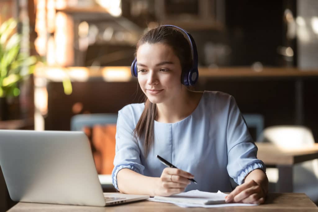 woman with headphones listening to online courses and taking notes