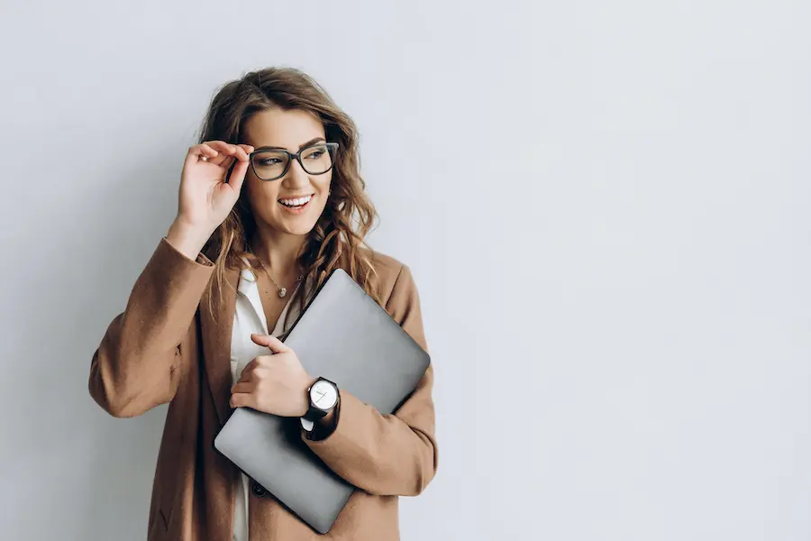 woman in a brown jacket holding her laptop and smiling