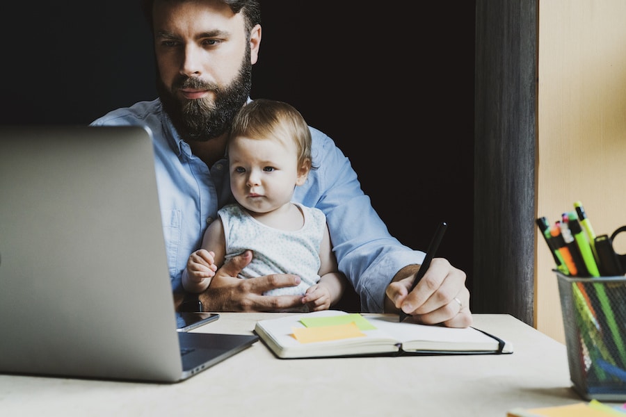 man with a beard holding his child in his lap while working