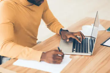 african american man in yellow sweater studying on his laptop