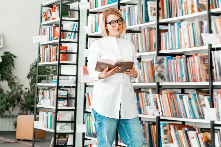 woman in a white shirt holding a book in a library