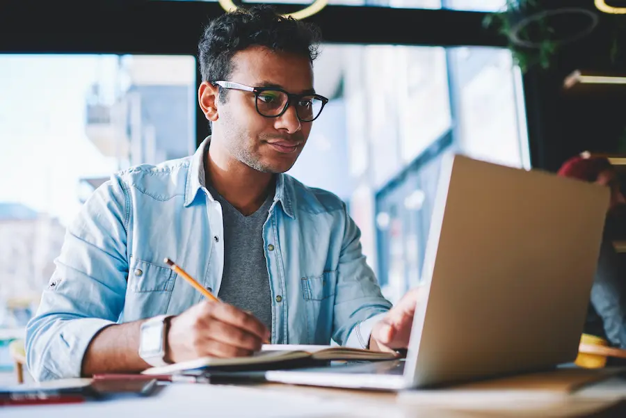 man in a denim jacket focused on taking notes with his laptop