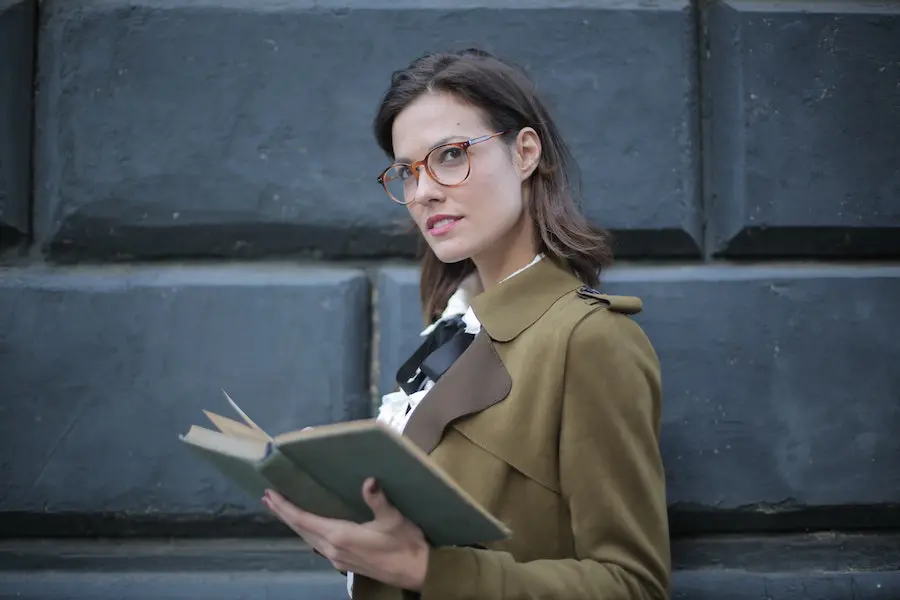 woman with eyeglasses holding a book and looking at the camera
