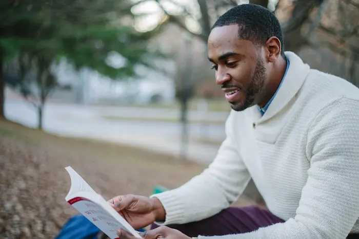 african american man in a white sweater reading a book outdoors