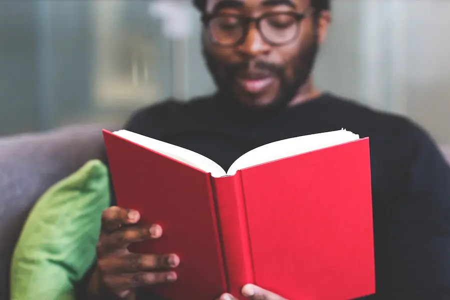 african american man with eyeglasses reading a book with a red cover