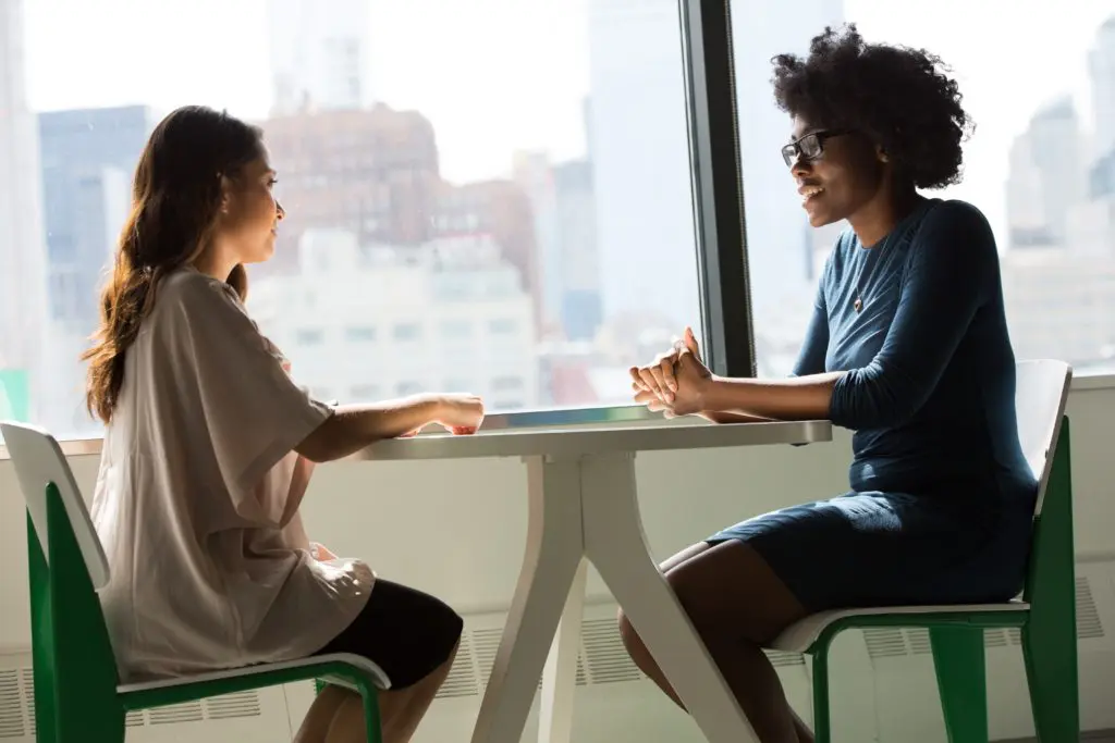 two women having a conversation at a table next to the window