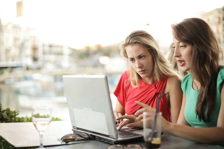 two women discussing details on a laptop in an outdoor coffee shop