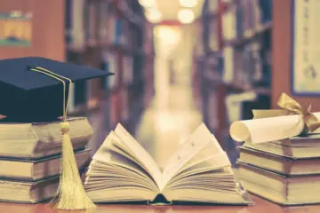 graduation hat and a diploma on top of a stack of books in a library