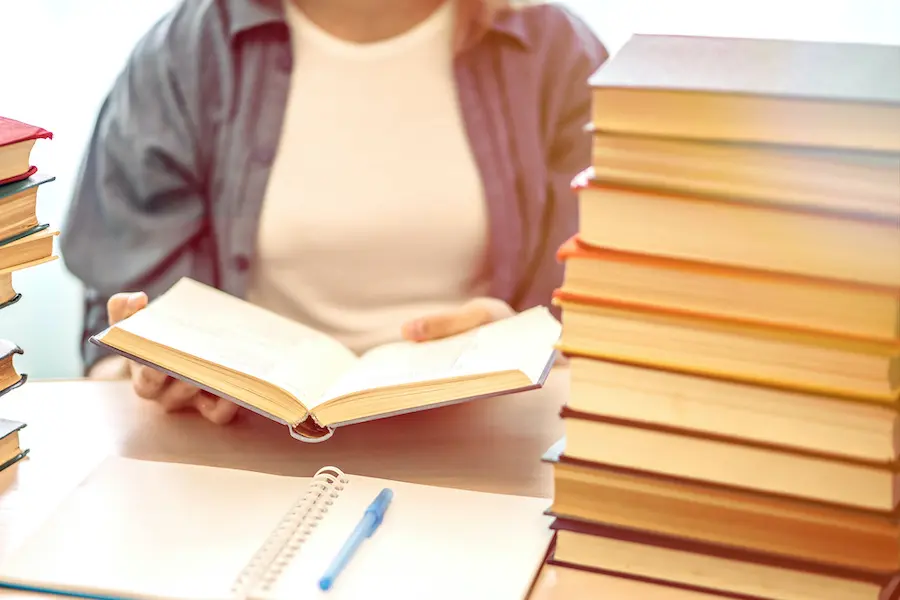 woman reading a book next to a large stack of books