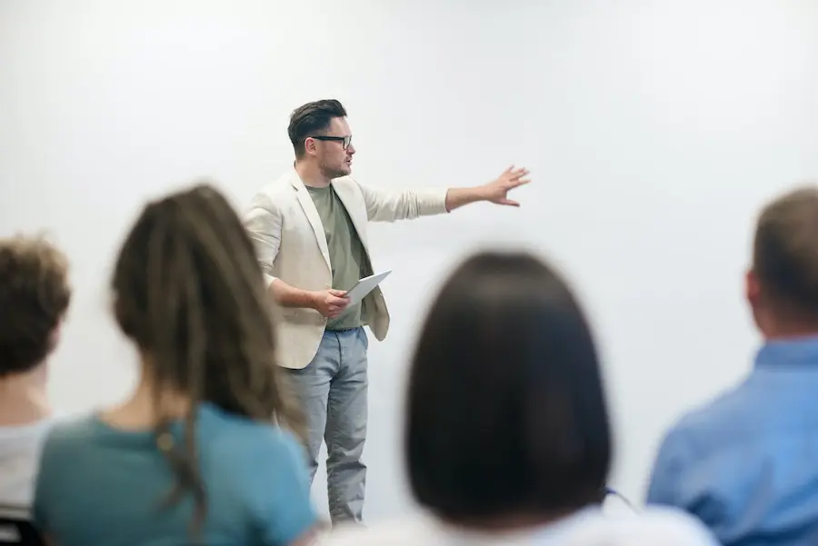 man in beige suit jacket holding a presentation on a whiteboard