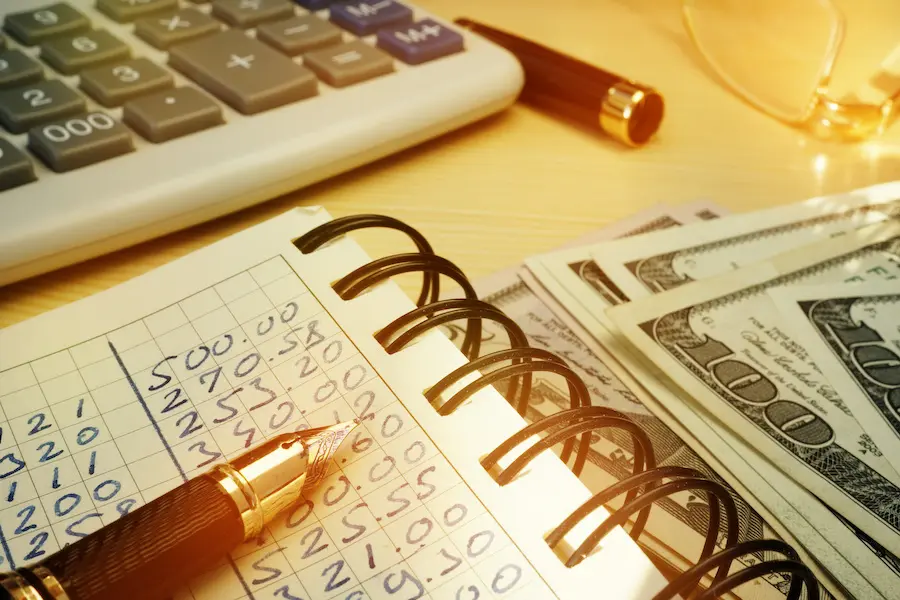 close-up shot of budget calculations in a notebook and a pile of dollar bills