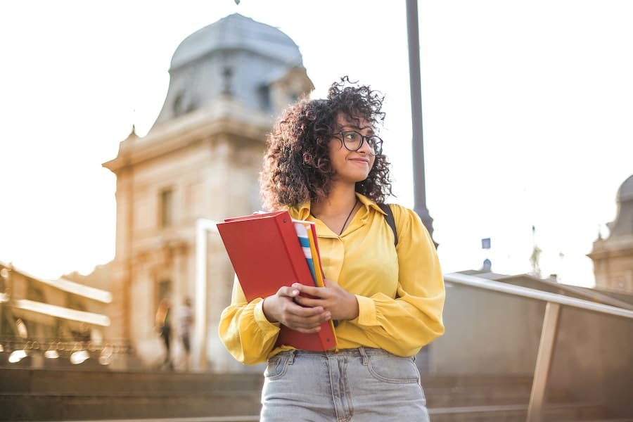 doing a second phd in australia woman in a yellow shirt smiling and holding a pile of notebooks and folders