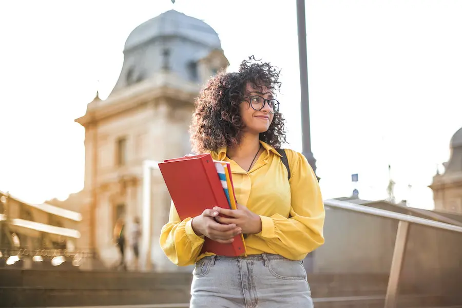 woman in a yellow shirt smiling and holding a pile of notebooks and folders