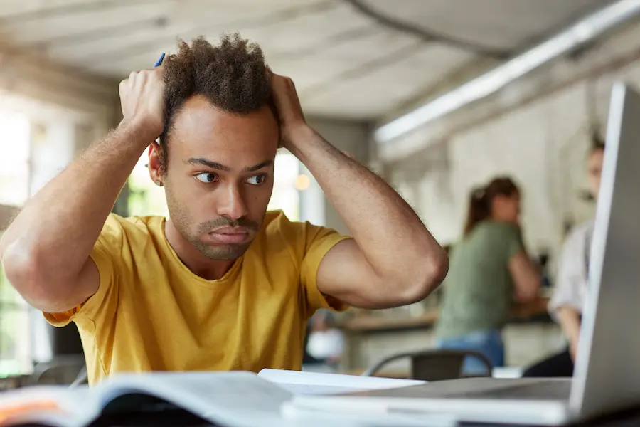 stressed out man in a yellow t-shirt looking at his laptop