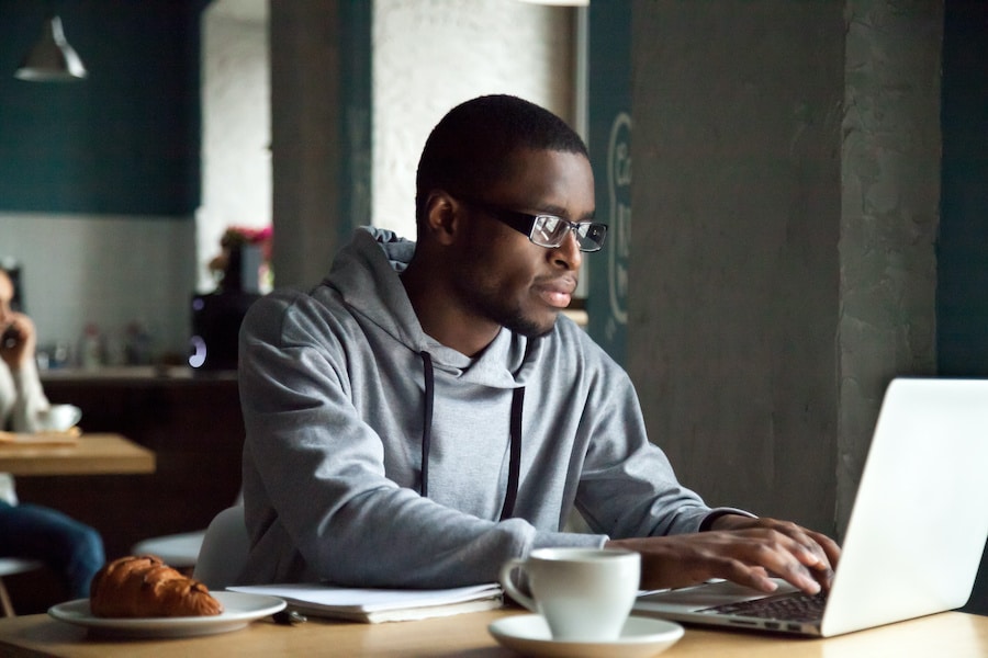 african american man with eyeglasses typing on his laptop in a coffee shop