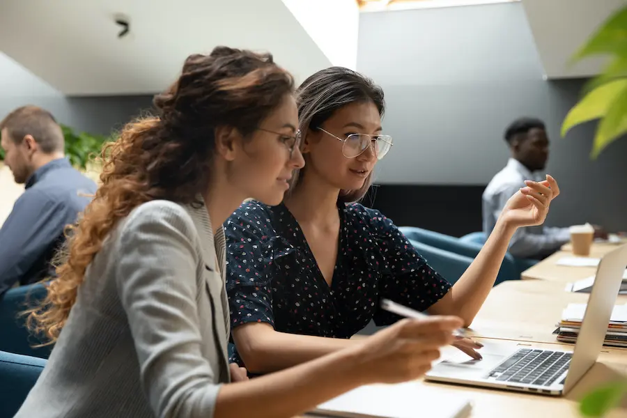 two women working together on a laptop in a shared office 