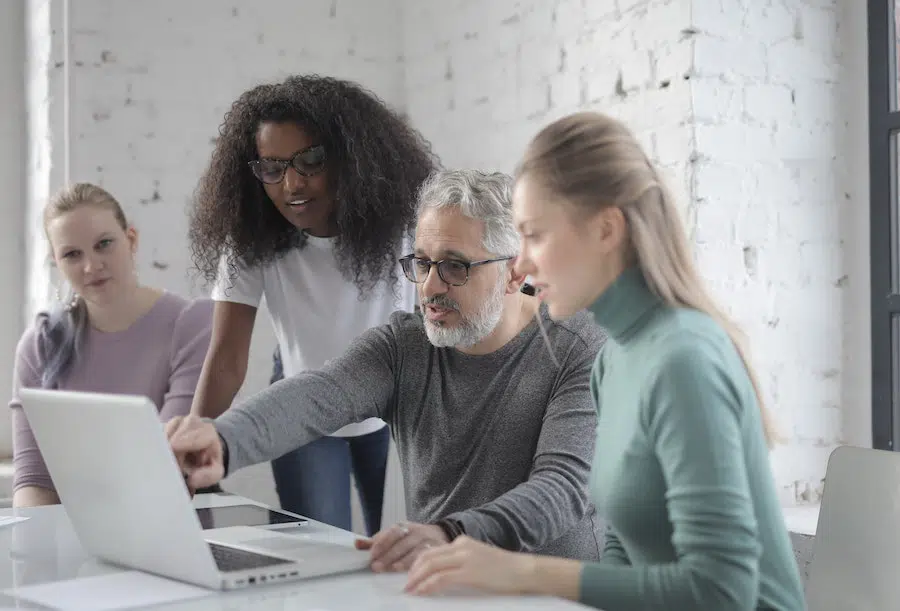 4 colleagues working together on a laptop inside a bright office