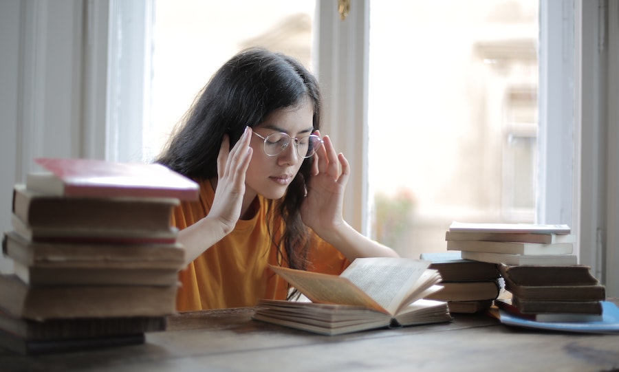 woman stressing out while studying with large stacks of book next to her