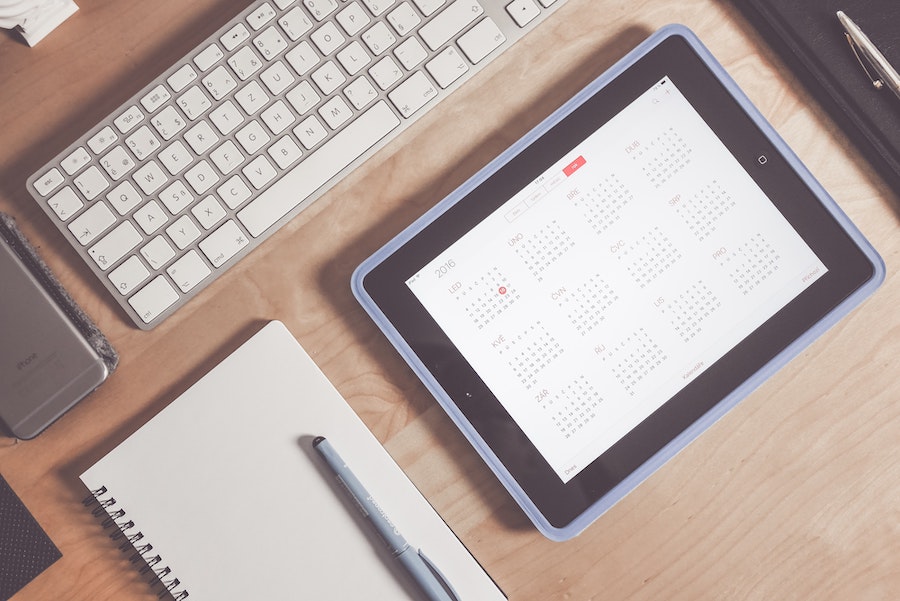 top view of a calendar on a tablet with a notebook, keyboard, and phone nex to it