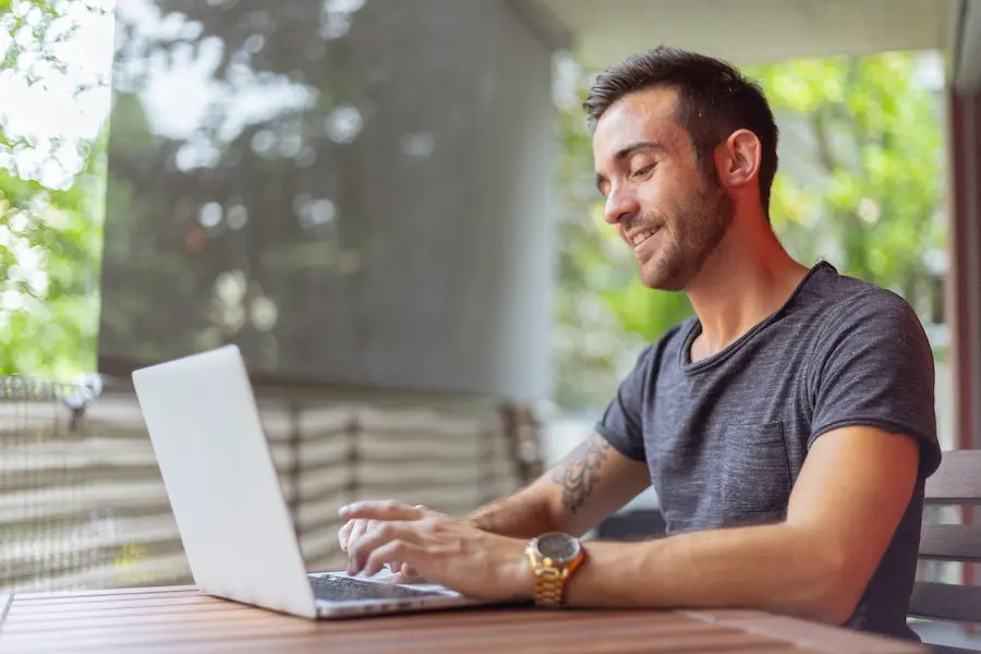 man with a golden watch and an arm tattoo typing on his laptop