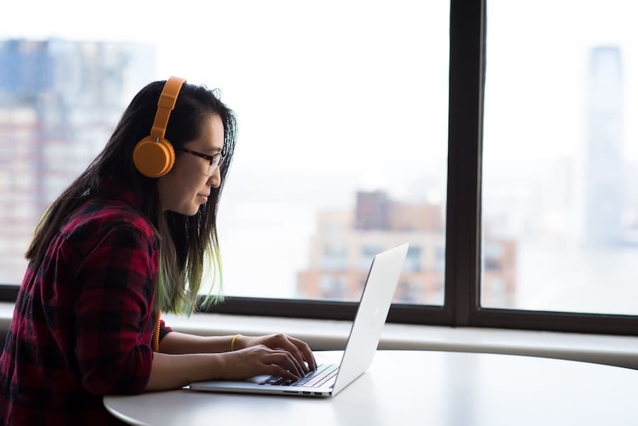 woman with orange sunglasses typing on her laptop next to a big window