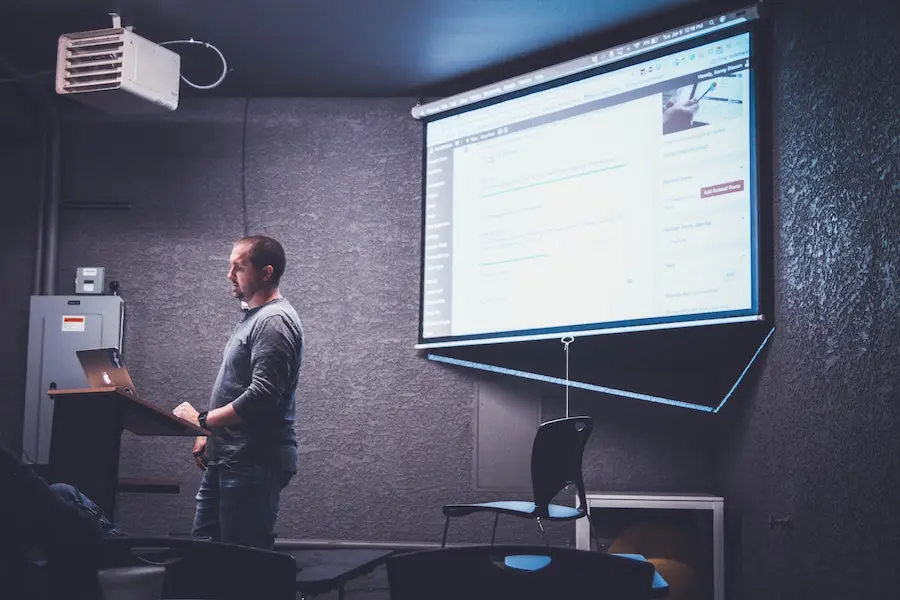 man with short hair holding a powerpoint presentation in front of a class