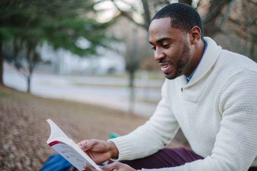 african american man in white sweater reading a book outdoors