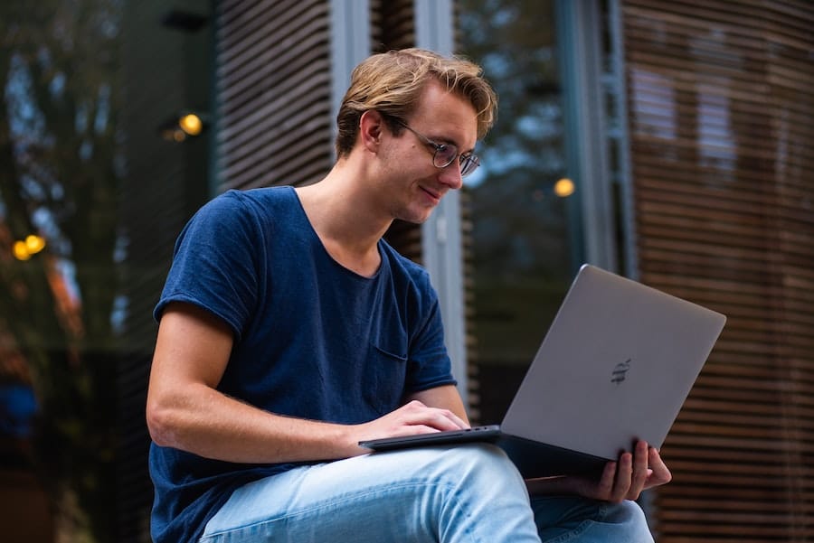man with light hair and eyeglasses smiling and working on his laptop