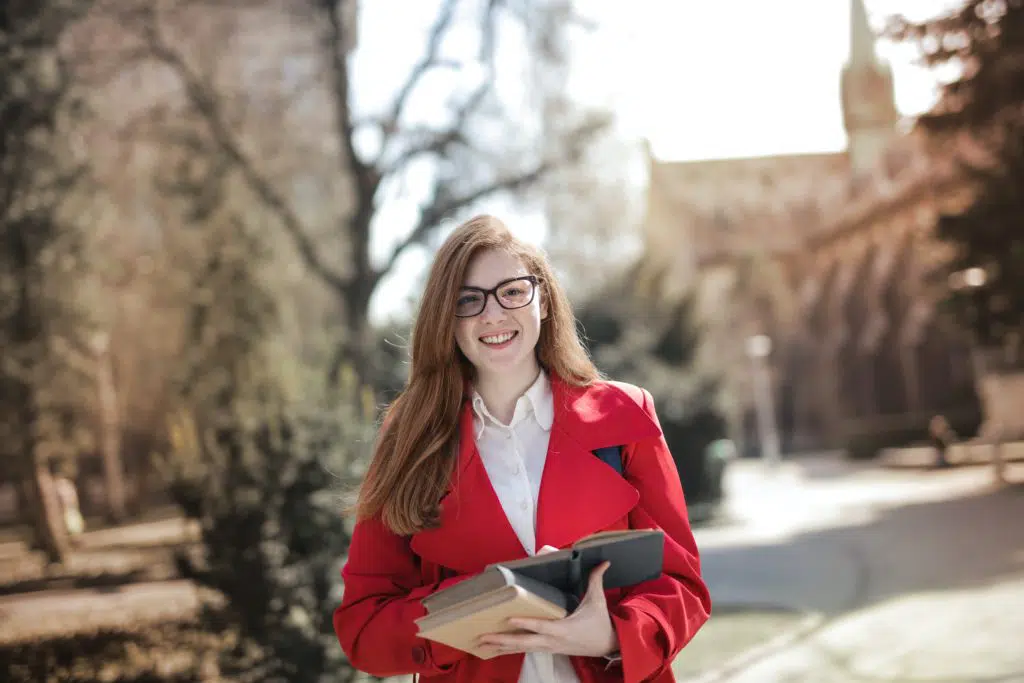 woman in a red coat holding books and smiling at the camera